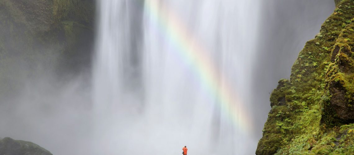 Rear view of person standing at foot of waterfall, moss-covered rocks and waterfall.